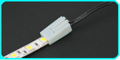 Weier LED-Verbinder mit Klemme, der eine LED-Leiste mit schwarzen Kabeln verbindet.