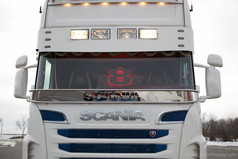 Beleuchtetes Scheibengitter mit roter Ziffer 8 hinter der Windschutzscheibe eines weien Scania LKWs.