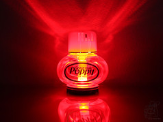 Poppy Lufterfrischer Flasche, von roter Beleuchtung durchdrungen, mit Reflexion auf dunklem Grund.