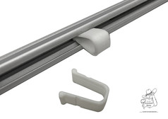 Weier U-frmiger Feststeller fr Gardinenschiene, teilweise in silberner Schiene eingesetzt, ein weiterer liegt daneben.