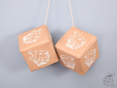 Beigefarbene Kunstleder-Wrfel mit weiem Lwenkopf-Stick, als Paar an Schnren hngend.