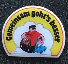 Scandi Pin mit Cartoon-Motiv: Groer Mann im LKW-Shirt hilft kleinem Mann im blauen Auto. Text: Gemeinsam geht