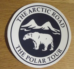 Blau-weier runder Aufkleber mit einem Polarbaer, Bergen und dem Schriftzug "The Arctic Road The Polar Tour".
