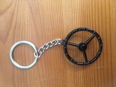 Schlsselanhnger mit schwarzem Old School Lenkrad und silbernem Schlsselring auf Holz.