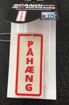 Rechteckiger cremefarbener Lufterfrischer mit rotem Rand und der Aufschrift PAHNG, in transparenter Verpackung mit weier Schnur.