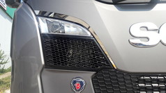 Glnzende Chrom-Bgen um den Scheinwerfer eines grauen Scania NG LKWs mit Scania Logo.