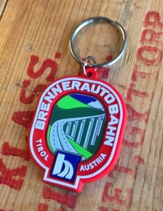 Roter Schlsselanhnger aus Gummi mit Brennerautobahn-Motiv, Brcke und Bergen. Beschriftet: "Brennerautobahn Tirol Austria".