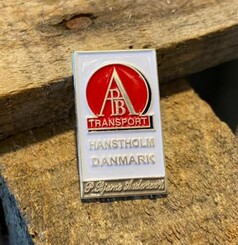 Scandi Pin: Weier Emaille-Pin mit rotem AB TRANSPORT Logo, HANSTHOLM DANMARK und P. Bjarne Andersen Schriftzug.
