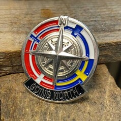 Ein runder Scandi Pin aus Metall mit Kompassrose, roten, blauen, weien und gelben Flaggenmotiven und dem Schriftzug "GOING NORTH".