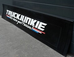 Schwarze Gummi-Heckschrze mit weiem 3D-TRUCKJUNKIE Schriftzug, farbigen Streifen und Montagekante.