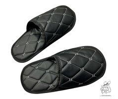 Ein Paar schwarze Kunstleder-Pantoffeln mit hellgrauen Steppnhten.