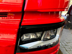 Schwarze Kunststoff-Blende fr Scania NG Scheinwerfer, auf rotem LKW, mit Schlitz-Design.