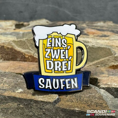 Emaille-Pin in Form eines Bierkrugs mit gelbem Krug, weiem Schaum und blauem Banner. Aufschrift: EINS, ZWEI, DREI SAUFEN.